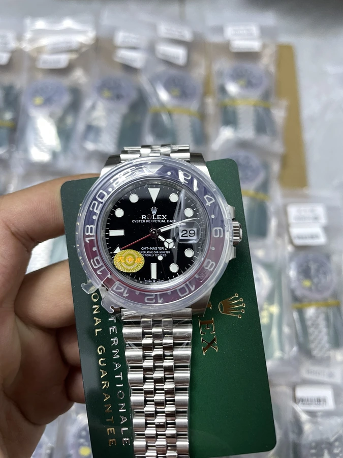 Black dial watch with silver bracelet and round hour markers, photographed in hand on a green presentation card.
