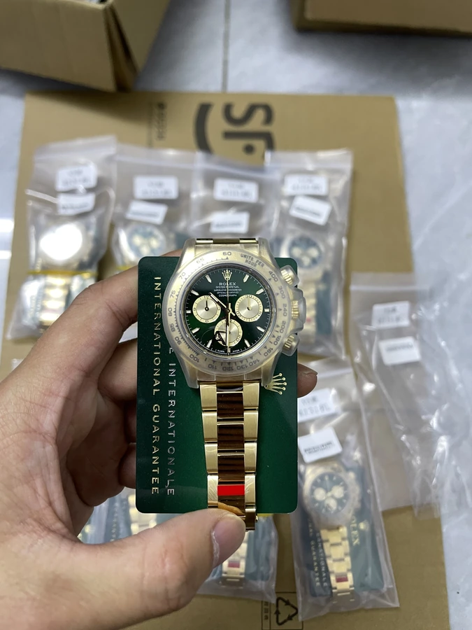 Gold-tone watch with a dark dial and two-tone bracelet, photographed in hand on a green presentation card.