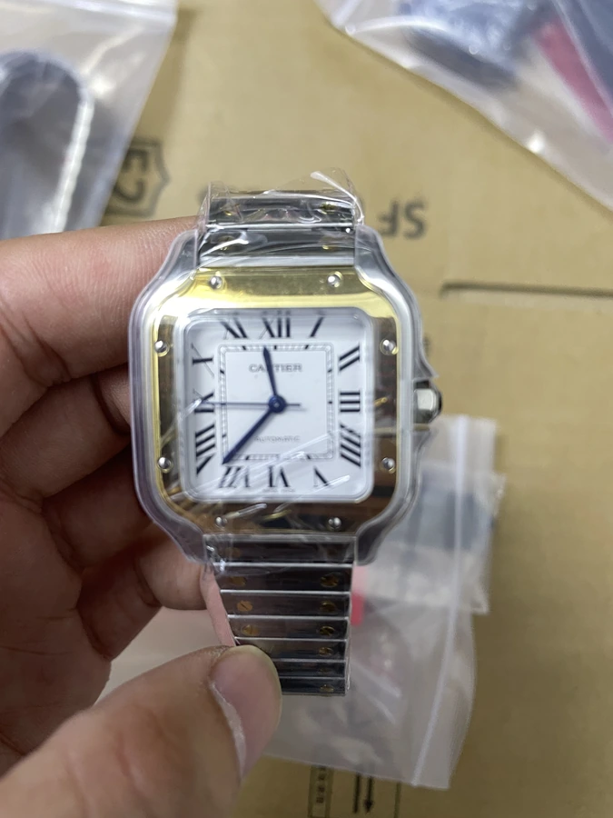 Square white dial watch with dark blue hands and a metal bracelet, photographed in hand with protective film.