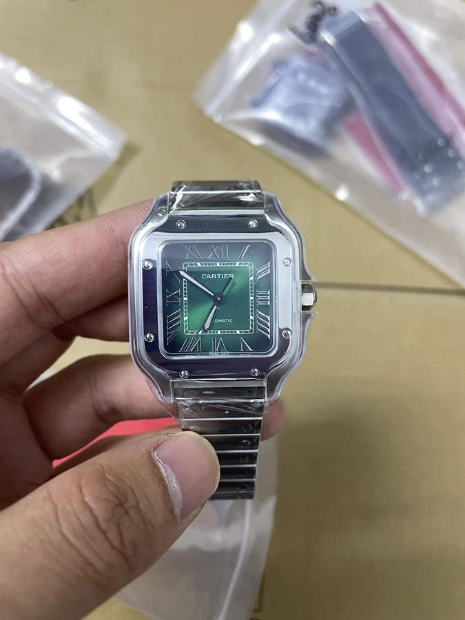 Square green dial watch with a silver bracelet, photographed in hand inside protective packaging.