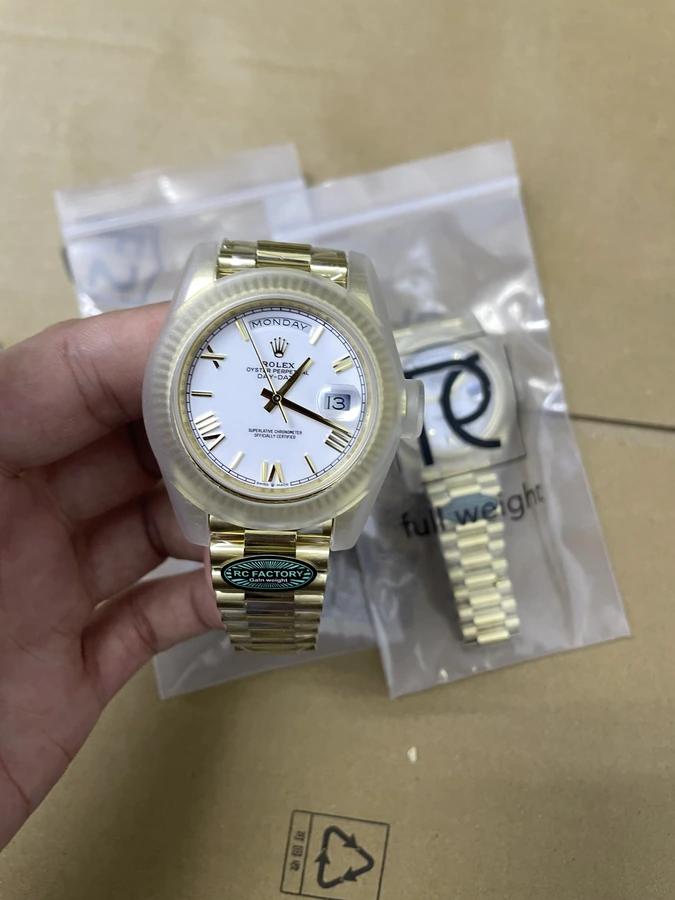 Light dial watch with a gold-tone bezel and bracelet, photographed in hand above protective packaging.