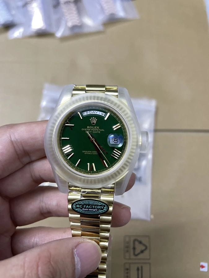 Green dial watch with a gold-tone bracelet, photographed in hand above protective packaging.