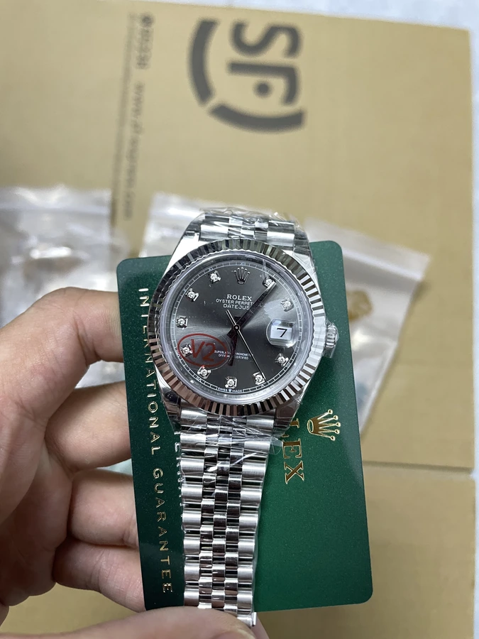 Dark gray dial watch with bright decorative hour markers, a fluted bezel and silver bracelet, photographed in hand.