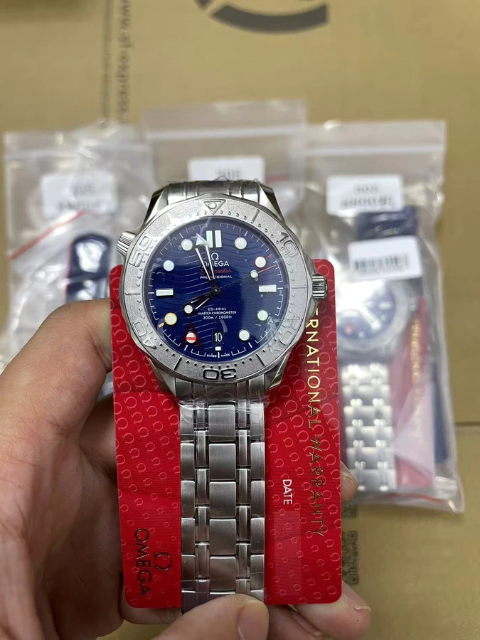 Blue dial watch with a silver bracelet and red presentation card, photographed in hand.