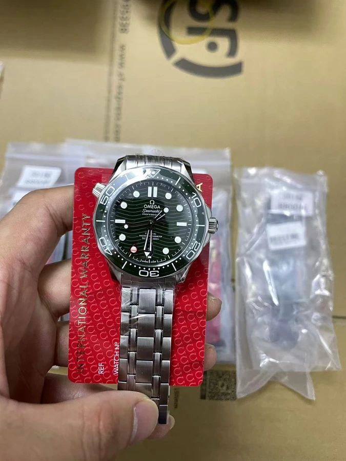 Green dial watch with a silver bracelet and red presentation card, photographed in hand.