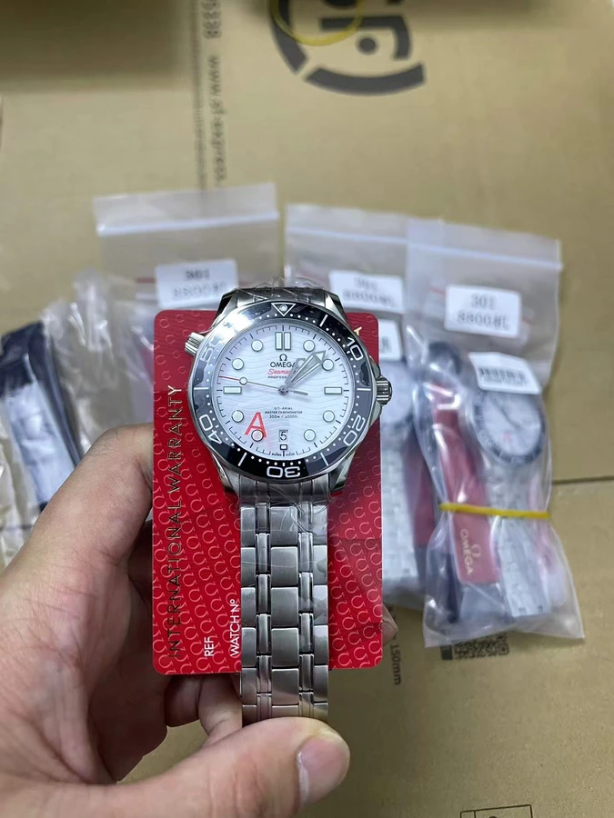 White dial watch with a black numbered bezel, silver bracelet and red presentation card, photographed in hand.