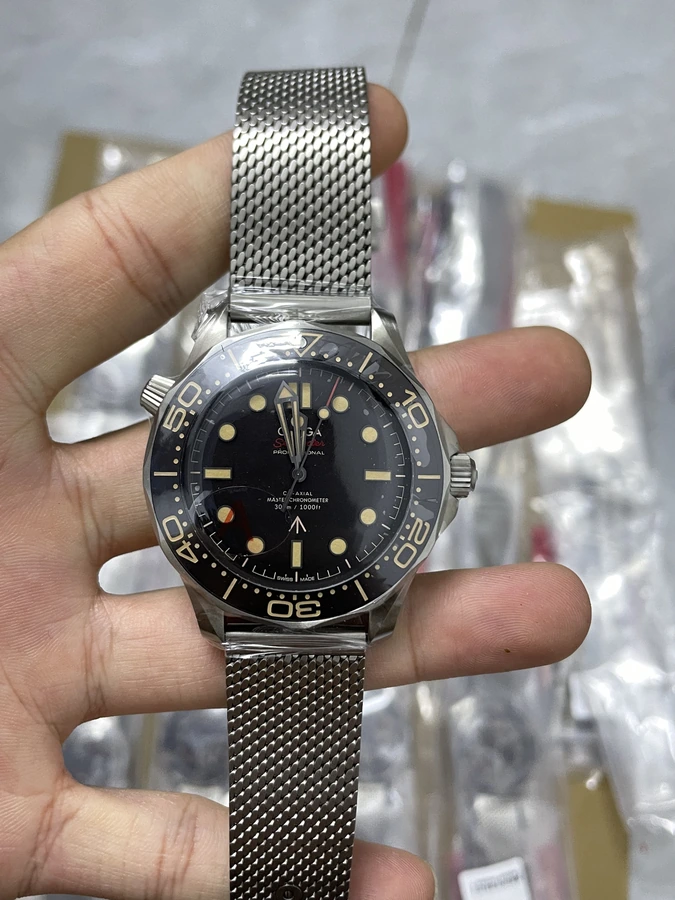 Black dial watch with a fine mesh bracelet, photographed in hand.